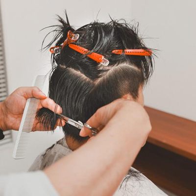 男性の後ろ髪をクリップで分け、コームとハサミで整えている手元(イメージ)