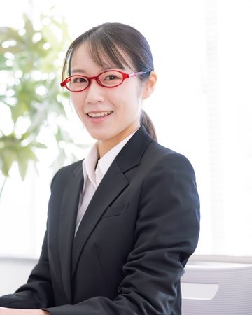 塾長のイメージ写真。机の向こうで笑顔を見せる、赤い眼鏡の女性(モデル)
