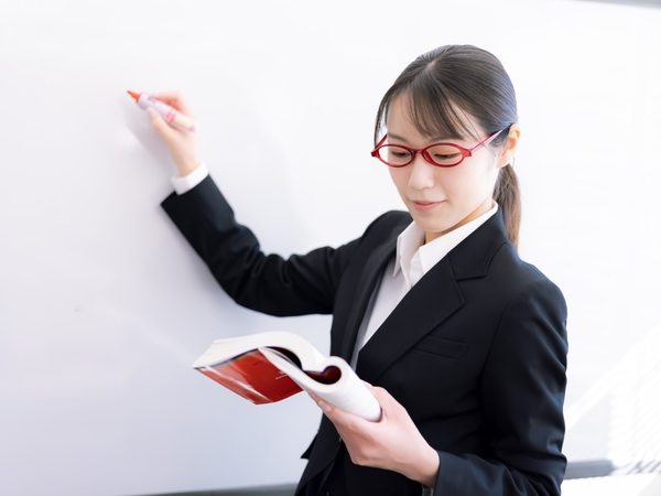 開いた教科書を見ながら、ホワイトボードに書く塾長(モデル)