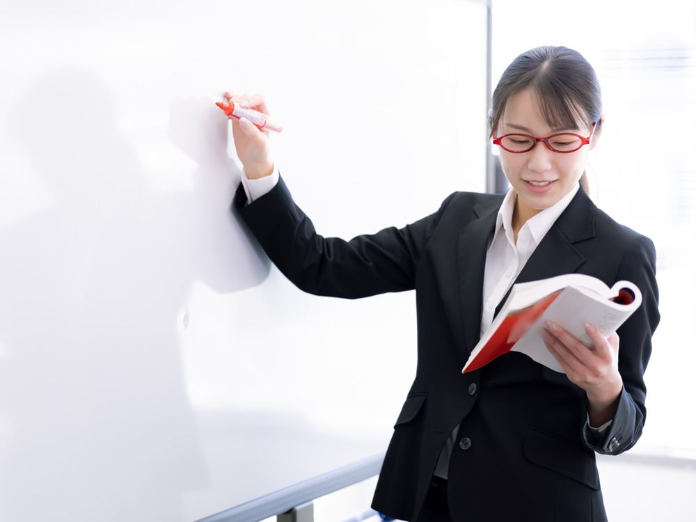 ホワイトボードの前に立ち、教科書を見ながら板書する塾長(モデル)