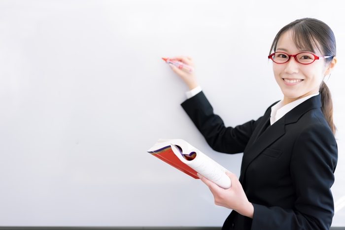 ホワイトボードに書きながら、こちらを向いて説明する塾長(モデル)