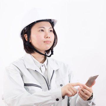 白いヘルメットをかぶった現場担当が、スマートフォンを確認している(モデル)