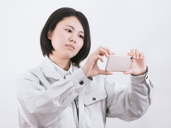 作業着の現場担当が、スマートフォンを横に構えて写真を撮っている(モデル)