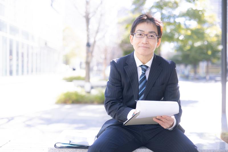代表のイメージ写真(モデル)。書類を手に、正面を向いてほほえむスーツ姿の男性